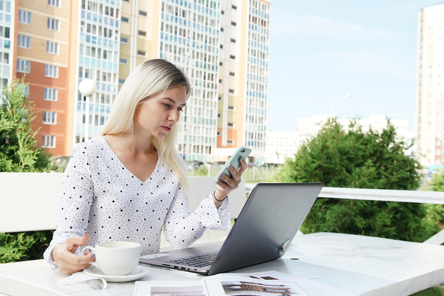 A girl on the street at a table with a phone and a laptop